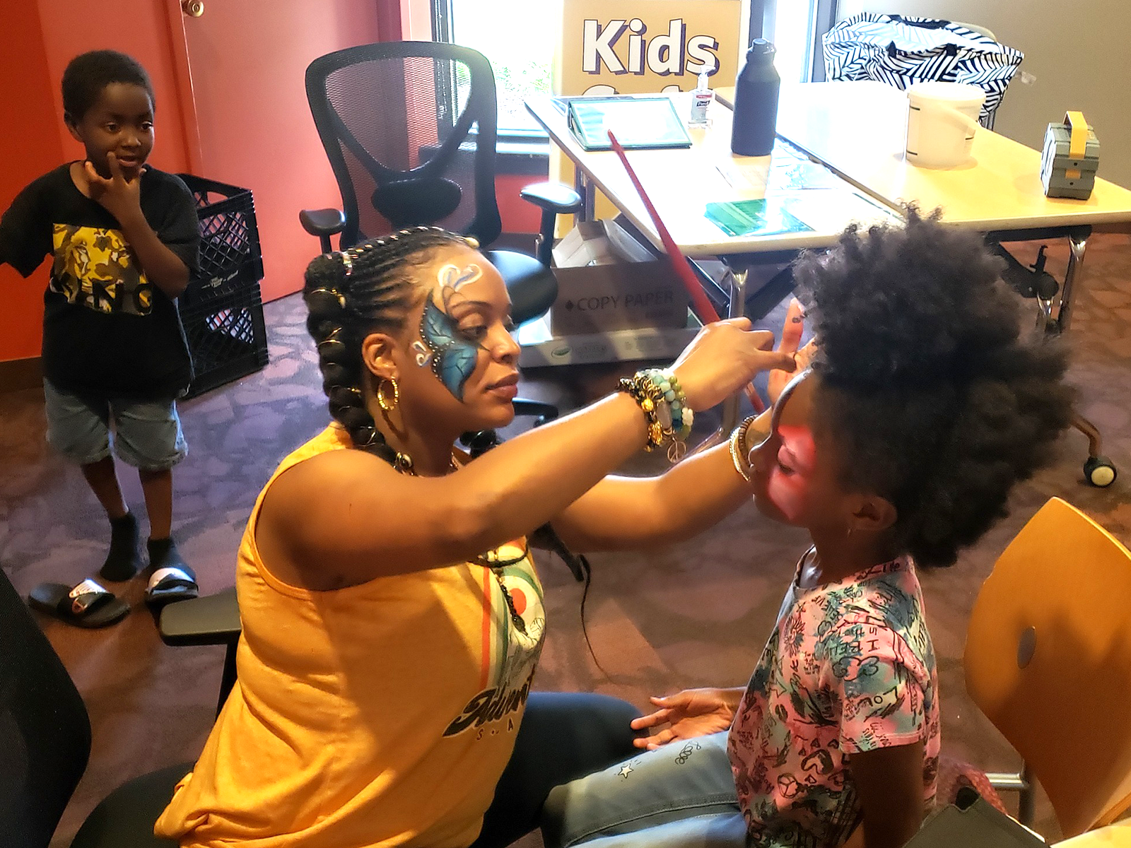 child getting their face painted while another watches