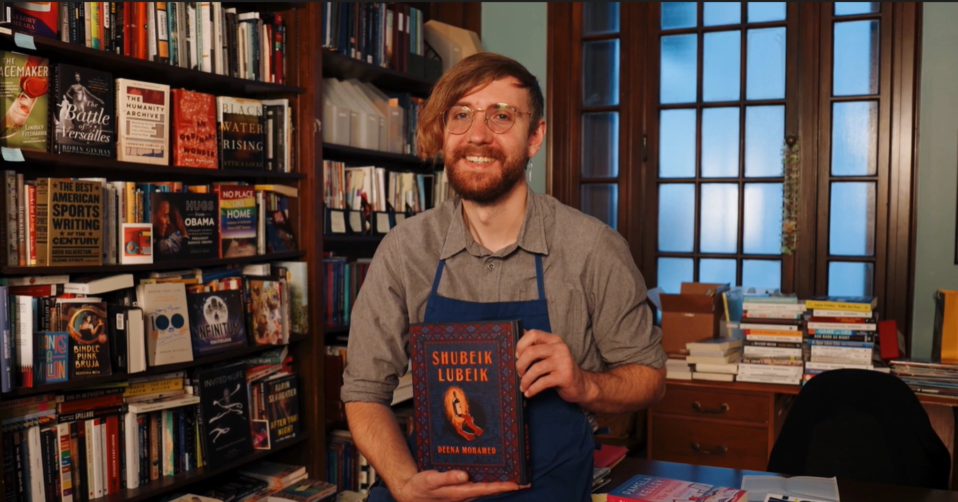person smiling in front of book shelves holding book