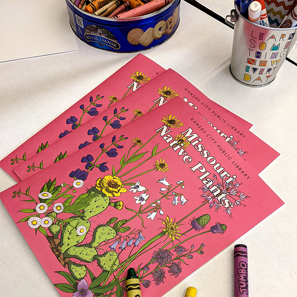 three coloring books stacked on table with crayons and markers