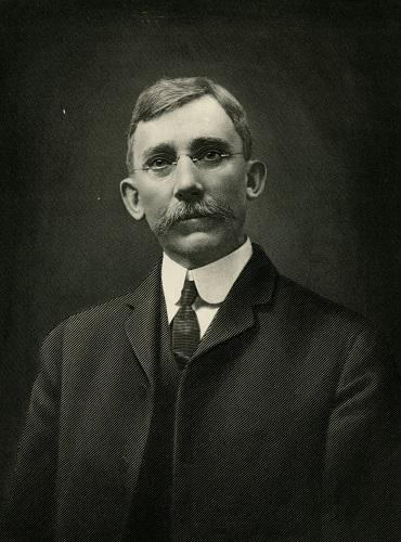 Portrait photograph of a man with oval glasses and mustache