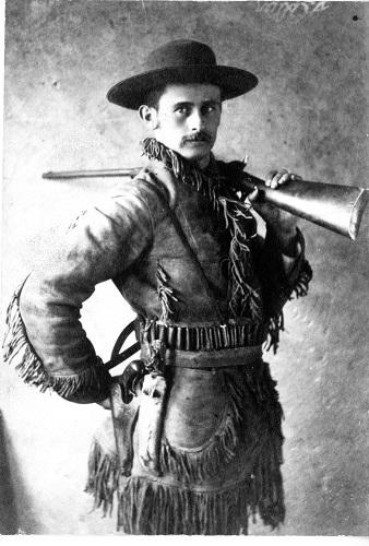 3/4 portrait photograph of a man in hat, skin clothing holding a rifle on his shoulder